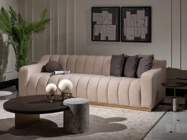 A cream-colored modern sofa featuring a sleek design with a luxurious gold plinth base, providing a sophisticated and elegant look suitable for contemporary interior settings.