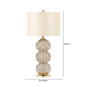 A sleek clear glass table lamp with a stacked ring-style base topped by a cream linen shade.