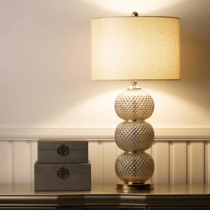 A sleek clear glass table lamp with a stacked ring-style base topped by a cream linen shade.