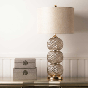 A sleek clear glass table lamp with a stacked ring-style base topped by a cream linen shade.