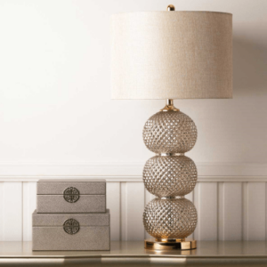 A sleek clear glass table lamp with a stacked ring-style base topped by a cream linen shade.