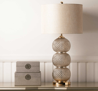 A sleek clear glass table lamp with a stacked ring-style base topped by a cream linen shade.