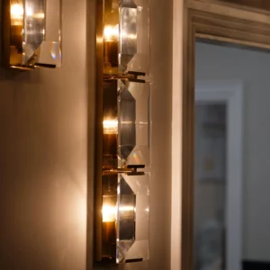 The Belgravia Wall Light exudes boldness and glamour, making it a standout piece for any room. Crafted with faceted crystal prisms and brass, it beautifully reflects and refracts light, reminiscent of emerald-cut diamonds. This luxurious crystal and brass wall light is the perfect addition to any space, combining timeless elegance with modern sophistication.