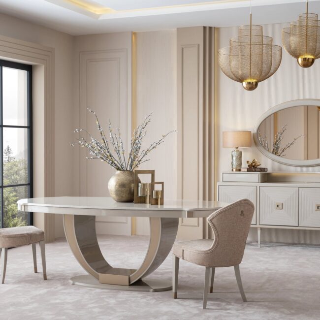 Sophisticated dining room featuring the cream Lusso dining set with a bronze-accented oval table, plush chairs, and a matching sideboard, complemented by golden decor and modern pendant lighting, in a neutral-toned interior.